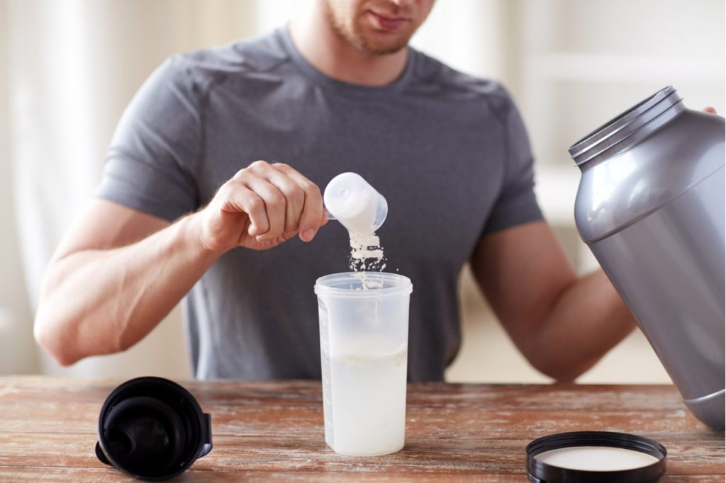 Close up of man with jar and bottle preparing protein shake.