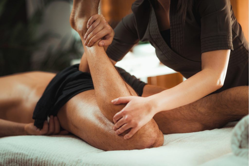 Physiotherapist massaging male patient with injured leg muscle.