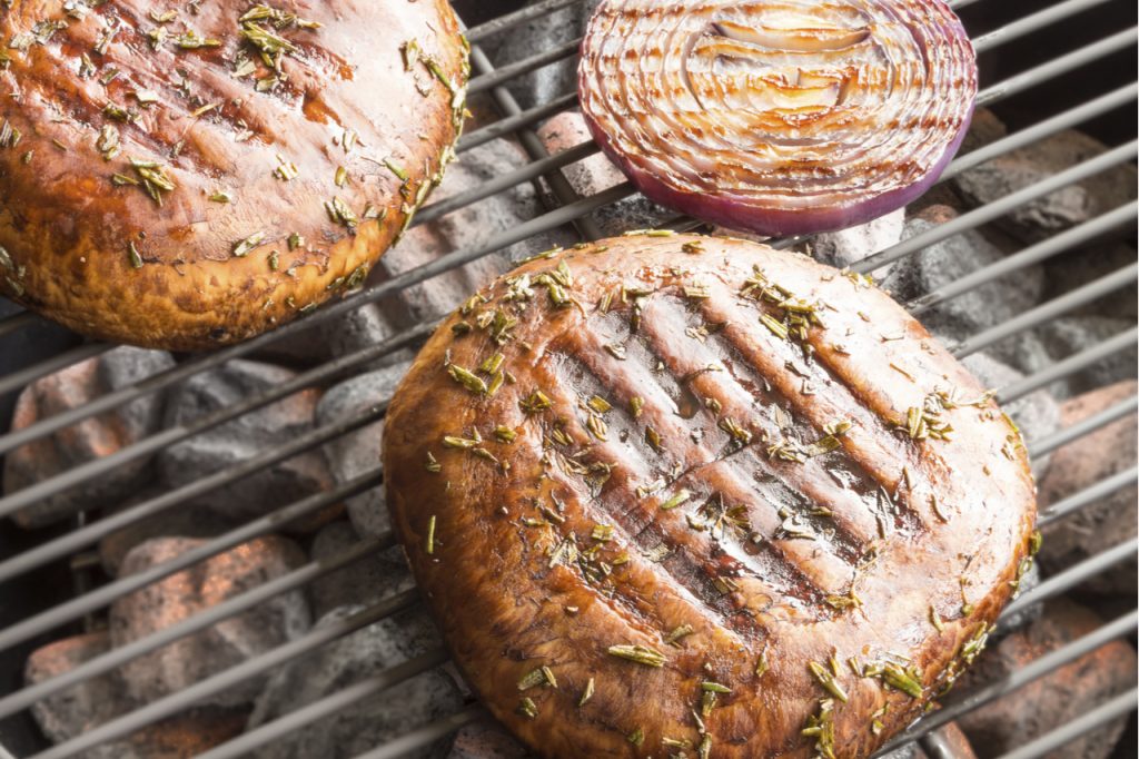 Two portobello mushrooms marinated and grilling with red onion.