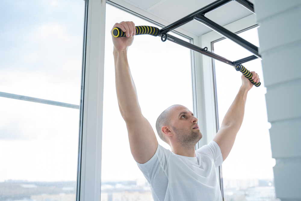 Man goes in for sports doing pull-up exercises on horizontal bar at his home