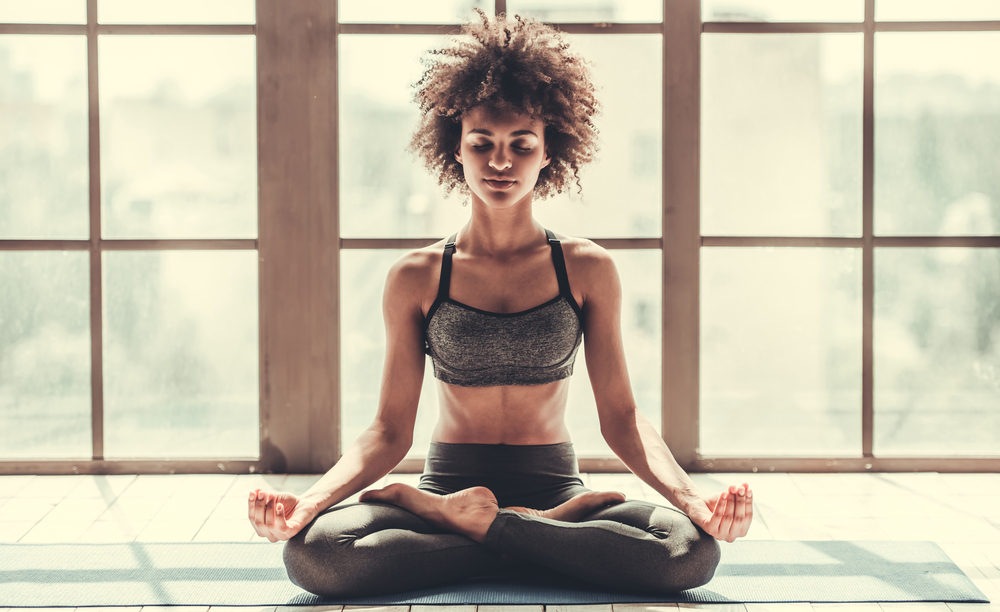 Afro American girl in sportswear is meditating while doing yoga