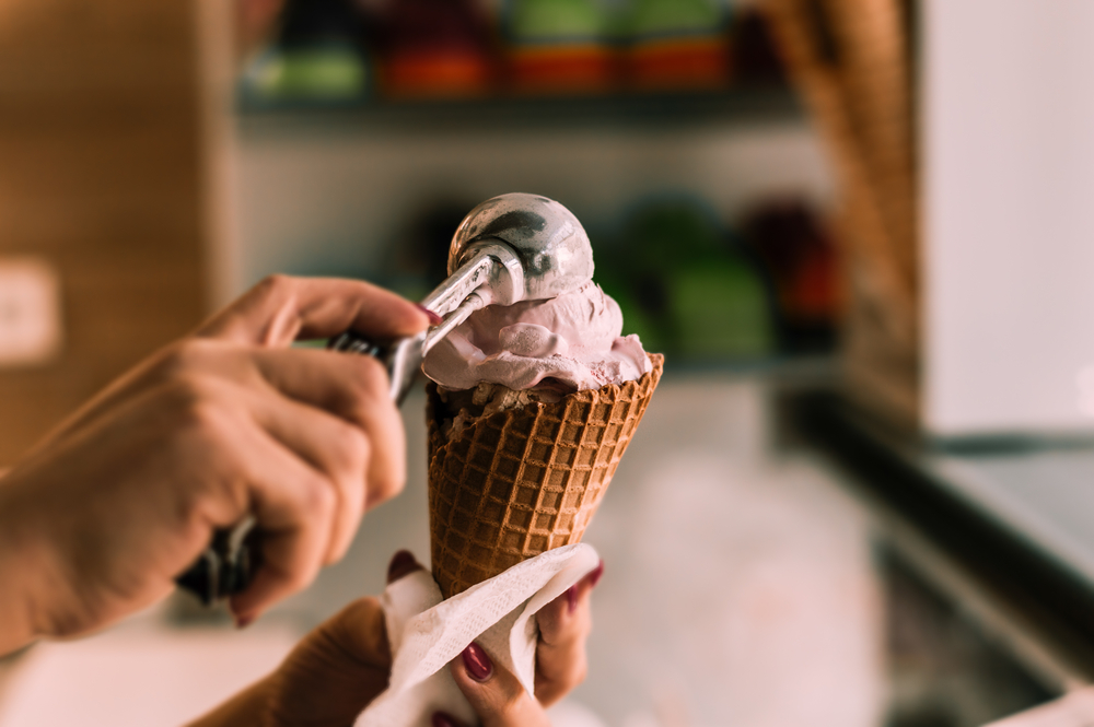 A scoop of ice cream being put on a sugar cone.