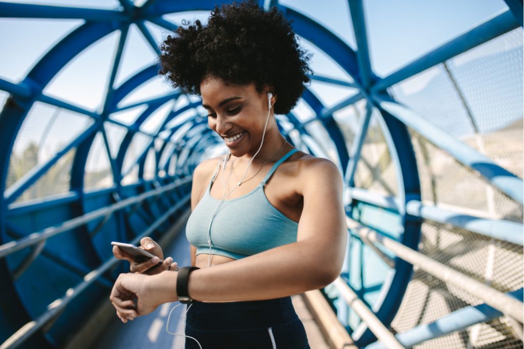 Fit female runner using smart watch and mobile phone to listen to music.