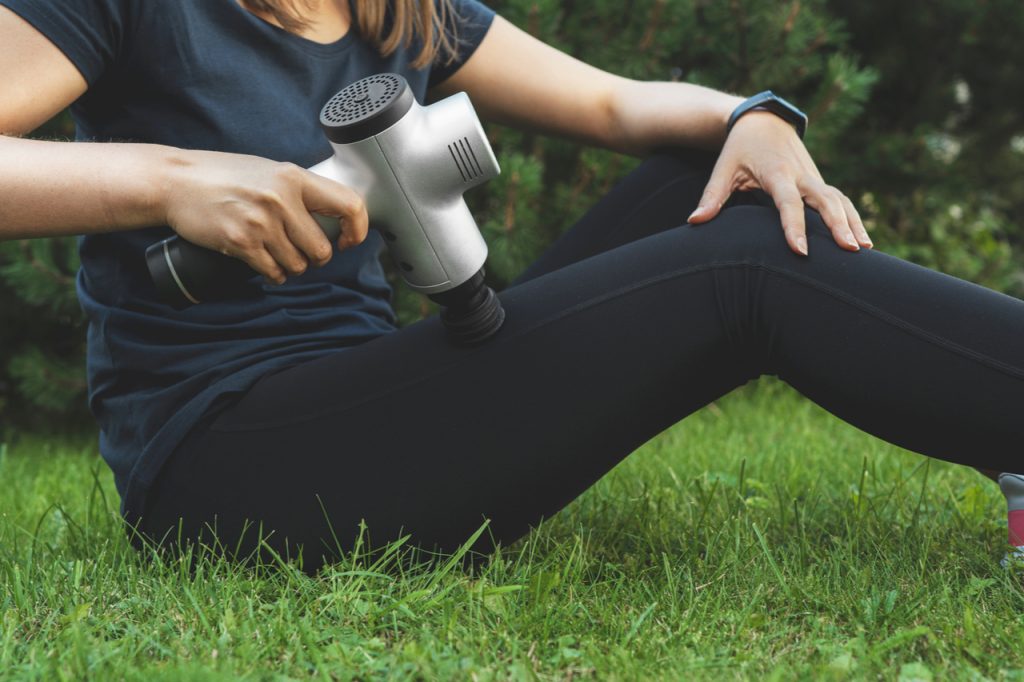 Woman massaging leg with massage percussion device after workout.