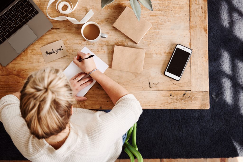 A woman writing thank you notes on her desk while having her coffee in the morning.