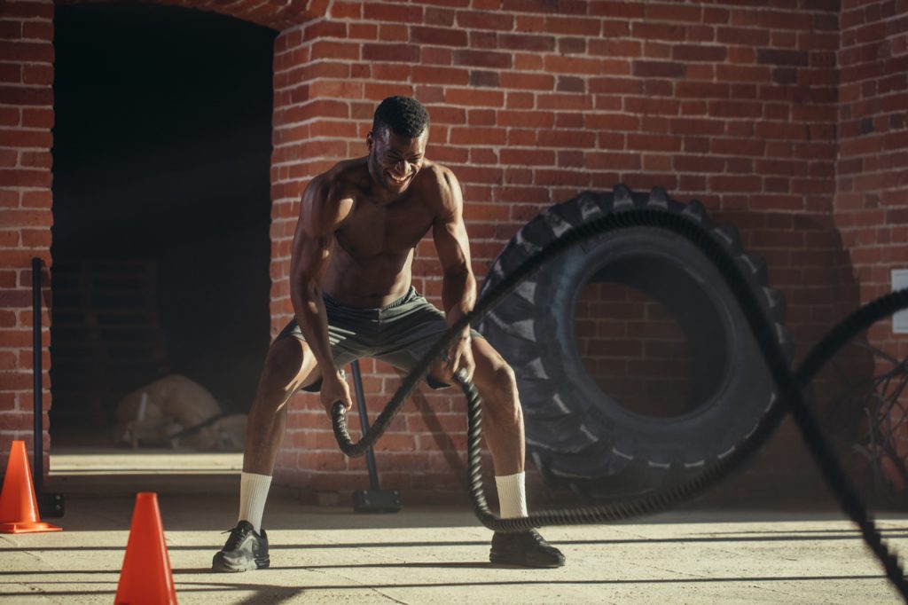 Muscular shirtless man is concentrated on the exercise with battle rope.