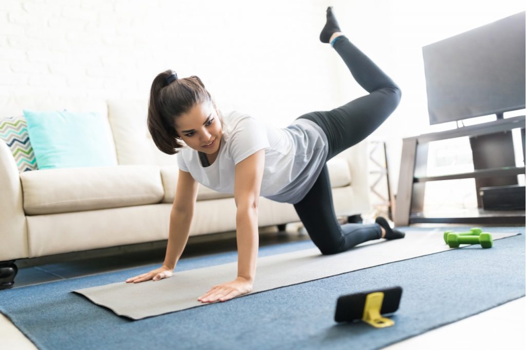 Woman repeating exercises while watching online exercise session on her smart phone at home.