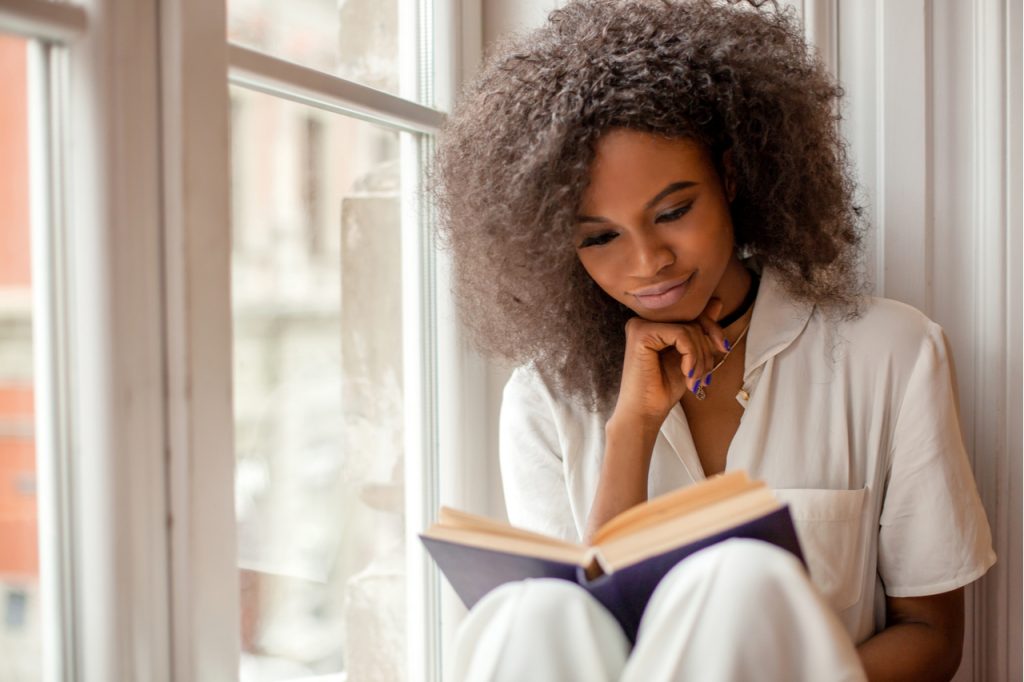 A beautiful african american woman reading a book by the window.