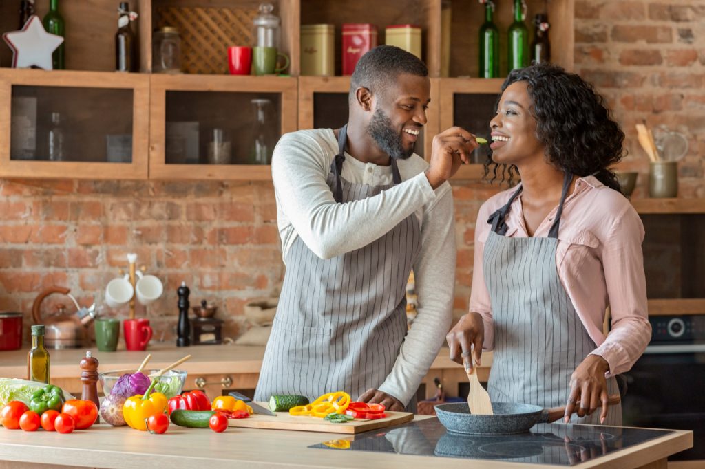 Man feeding his beautiful woman while cooking together at kitchen, empty space.