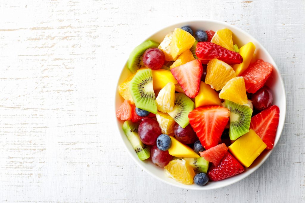 Bowl of healthy fresh fruit salad on wooden background.