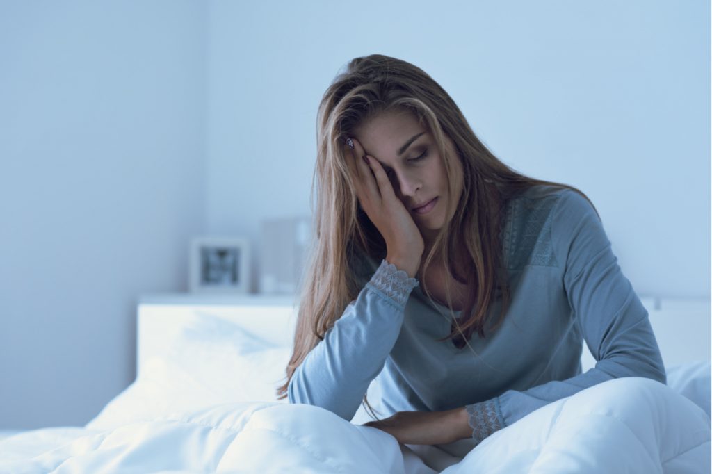 Woman awake in the night, she is touching her forehead and suffering from insomnia which is one of the signs and symptoms of depression.