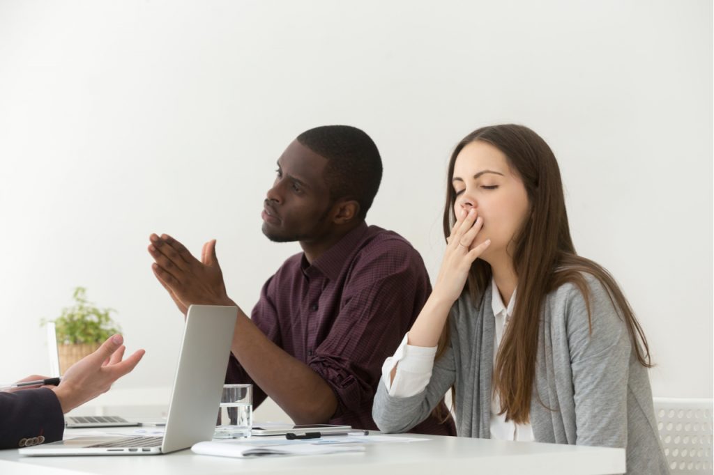 Woman yawning felling lethargic at the office meeting with diverse colleagues or partners.
