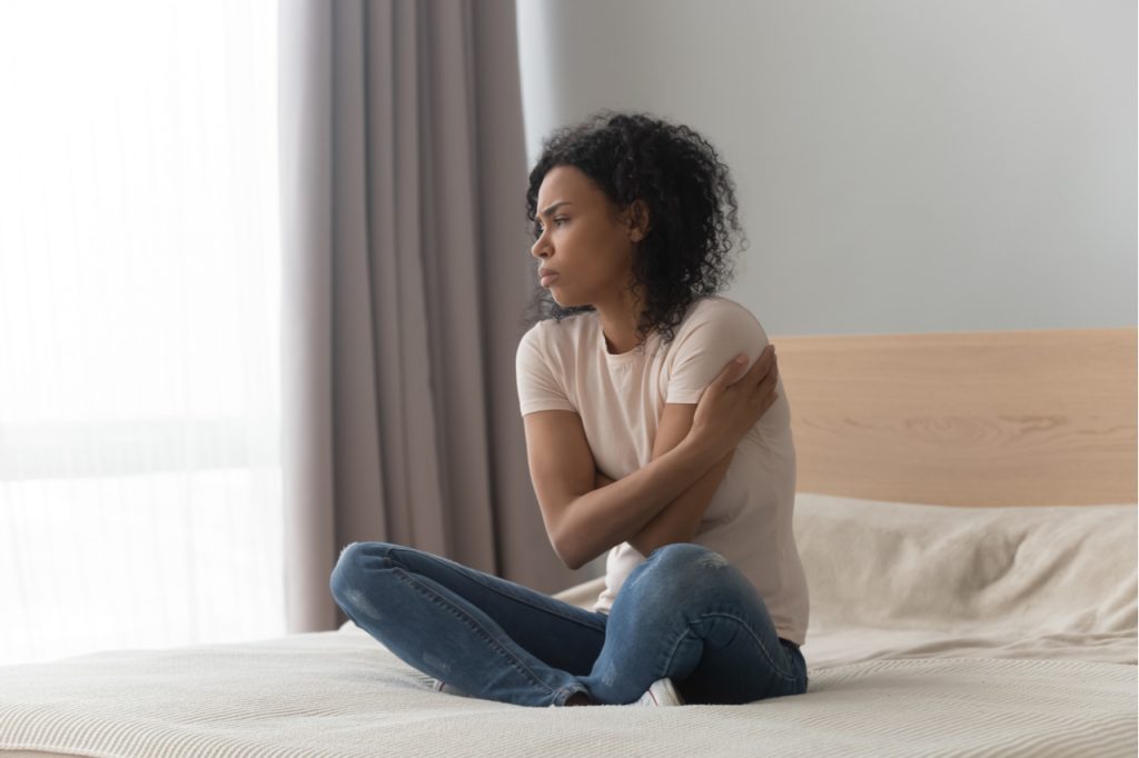 woman sitting in bed alone, hugging herself, feeling lonely.