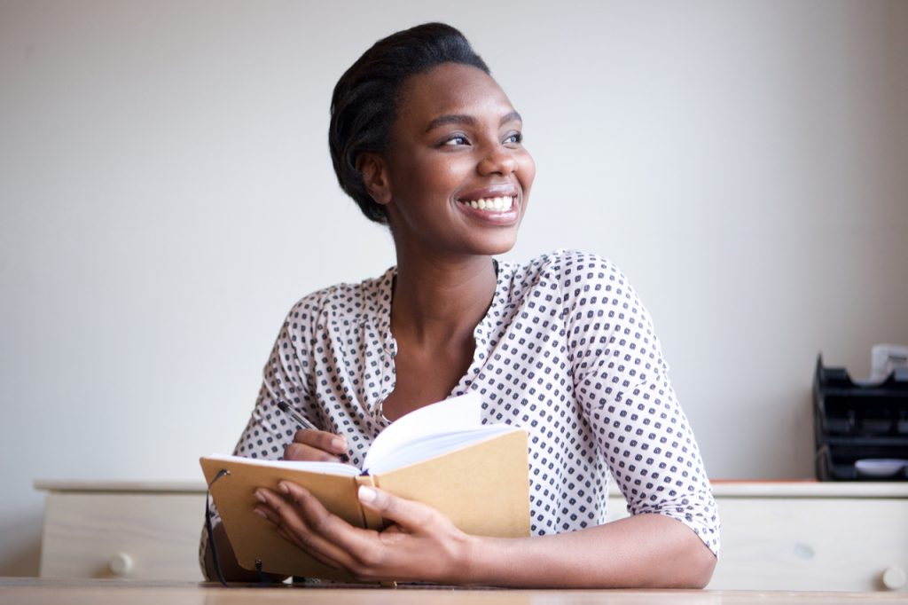 Portrait of smiling young black woman writing in journal at home.