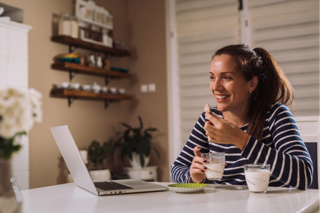 Woman enjoying her greek yogurt while working using a laptop.