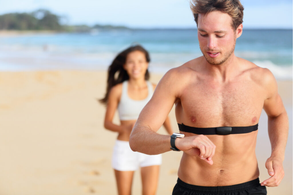 Handsome shirtless male runner working out outside by the ocean wearing heart rate monitor.