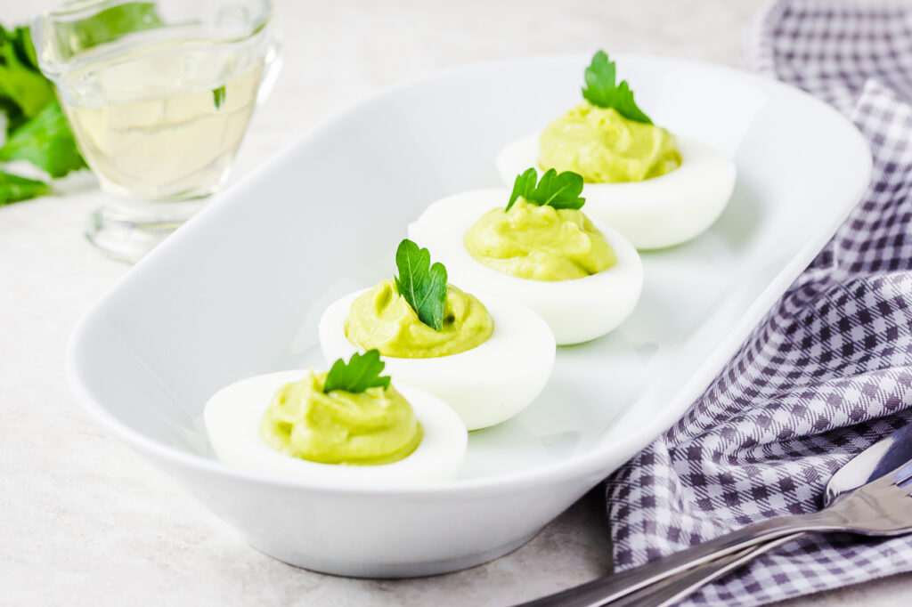 Avocado devilled eggs with parsley on white background.