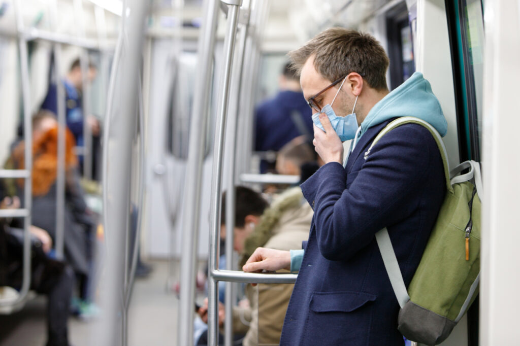 A man trying to avoid getting close to anyone on a train.