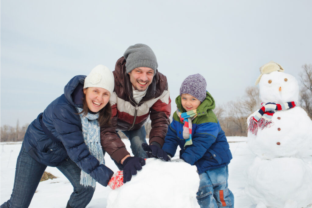 Happy beautiful family building snowman outside as part of their winter activities.