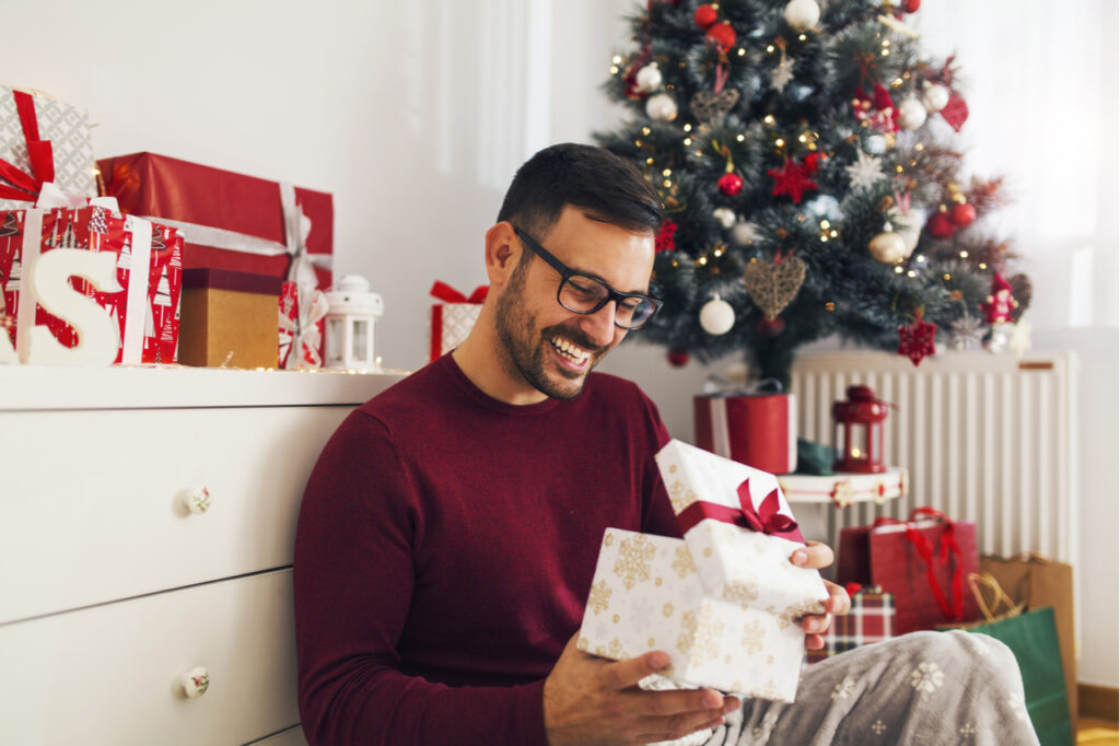 Smiling young man opening Christmas gift at a house with diy christmas arts and crafts.