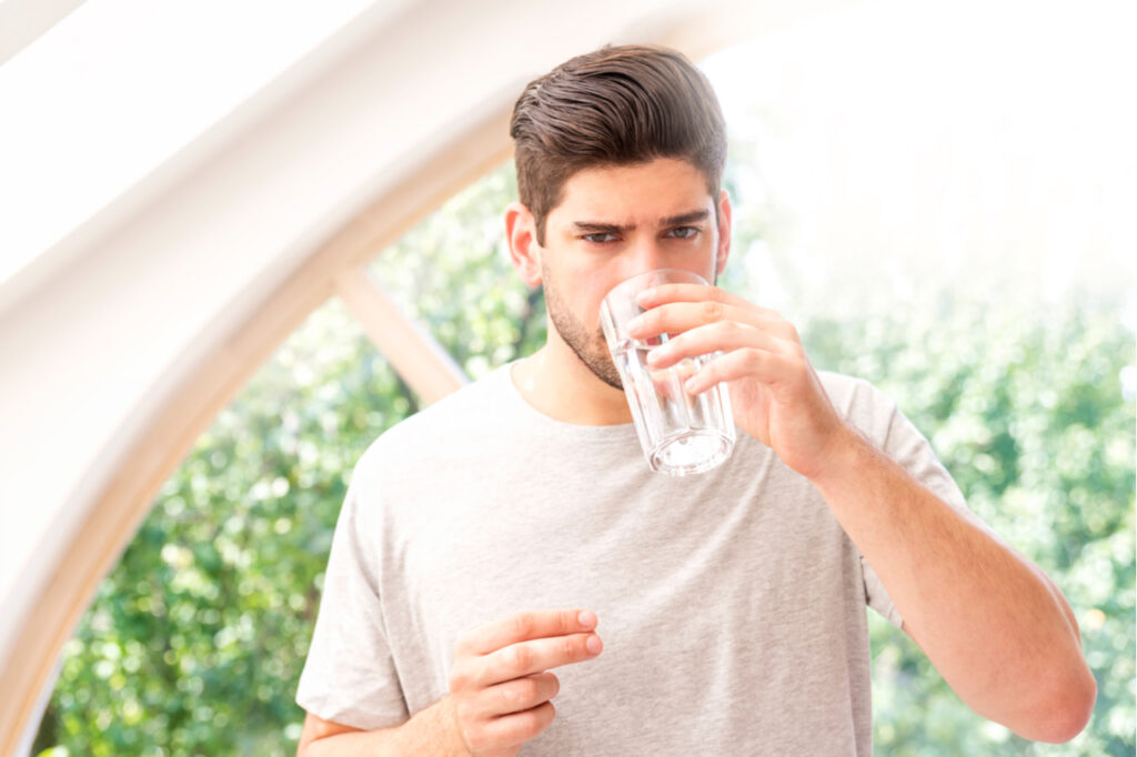 Handsome man holding a glass of water in his hand while taking pill.