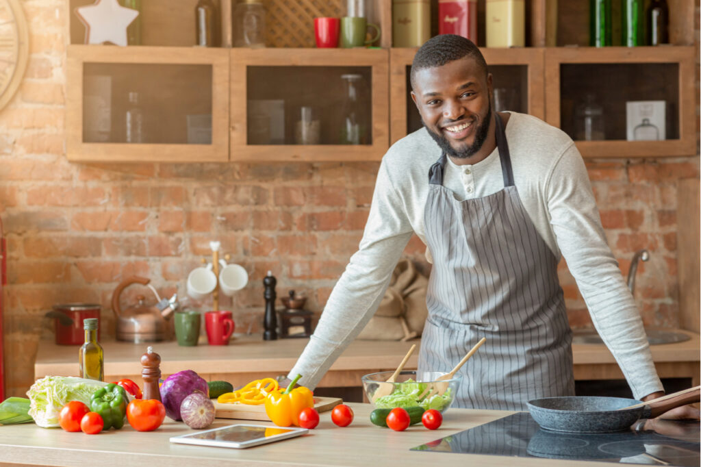 Attractive black positive man posing at kitchen while cooking dinner for his family, free space