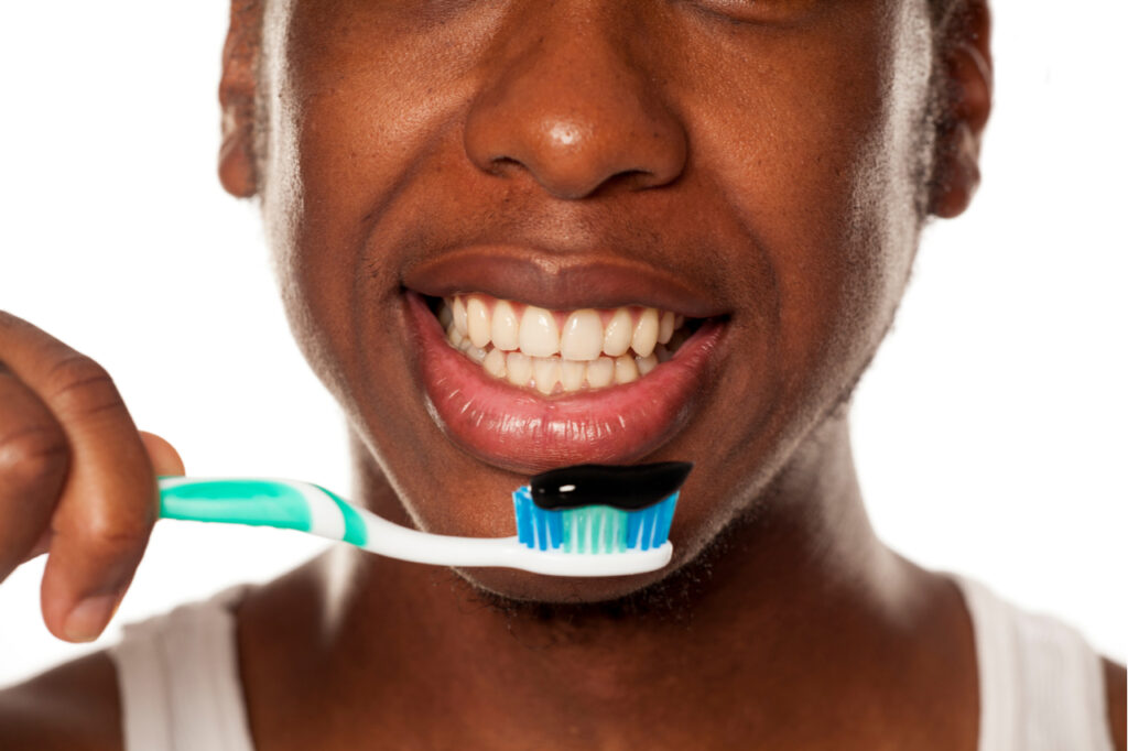 Happy looking man posing with toothbrush with activated charcoal toothpaste.