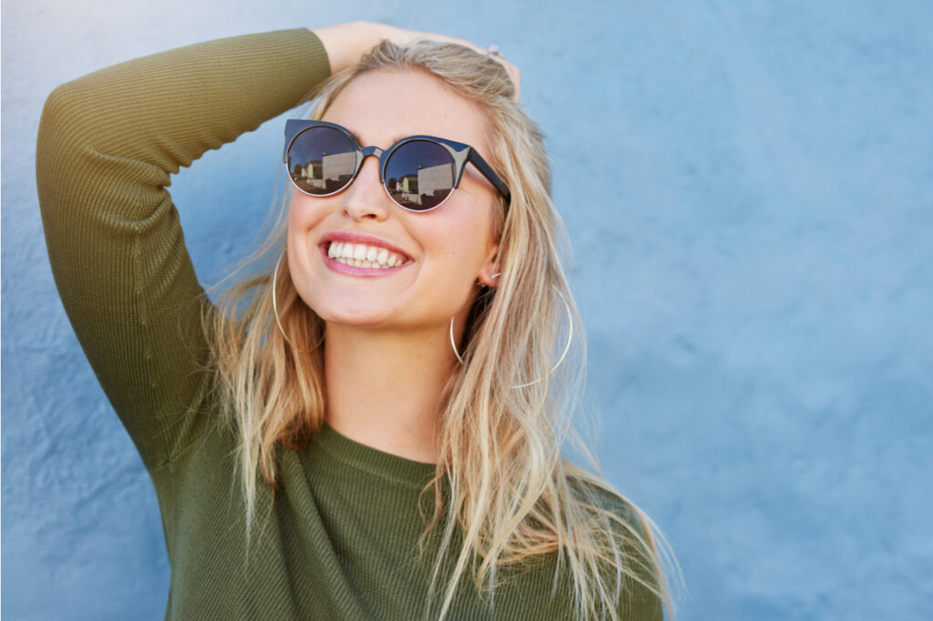 Blonde woman wearing shades smiling, thinking positively.	