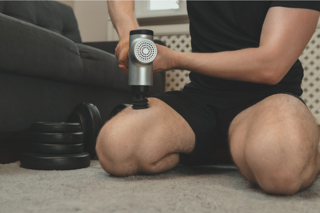 Man massaging leg with sonic handheld massage gun device.