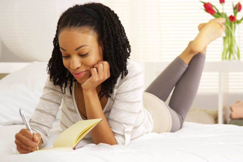Happy woman writing in her journal on the bed.