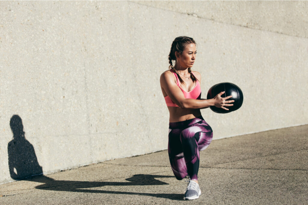 Sportswoman doing stretching exercise with medicine ball.
