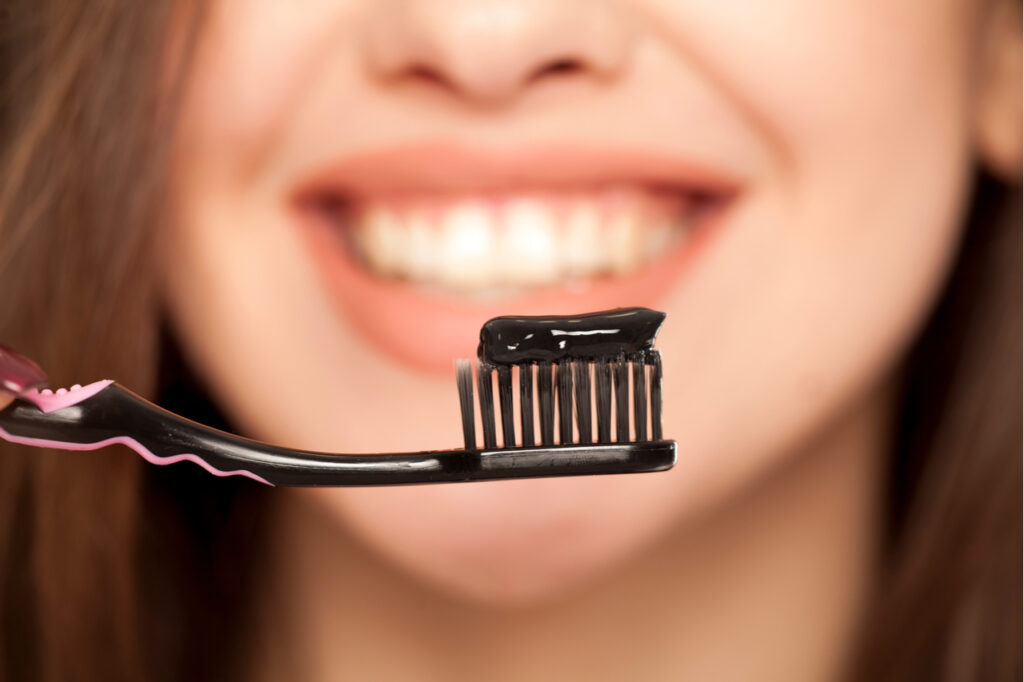 Young woman holding a black tooth paste with active charcoal, and black tooth brush. She uses activated charcoal infused toothpaste as part of her dental care.