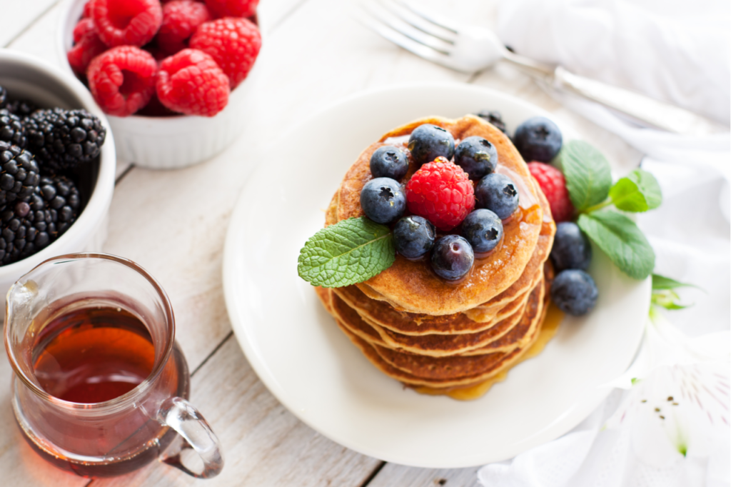 Stack of delicious paleo apple-cinnamon pancakes served with fresh berries, mint and maple syrup