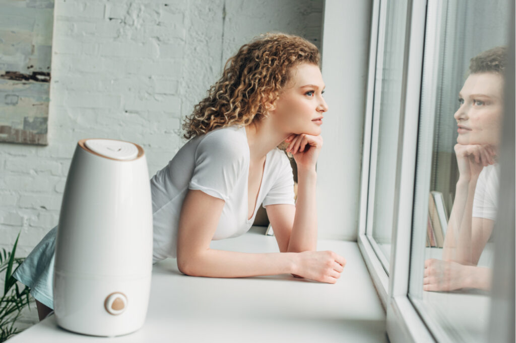 Beautiful girl with ultrasonic air purifier on windowsill.