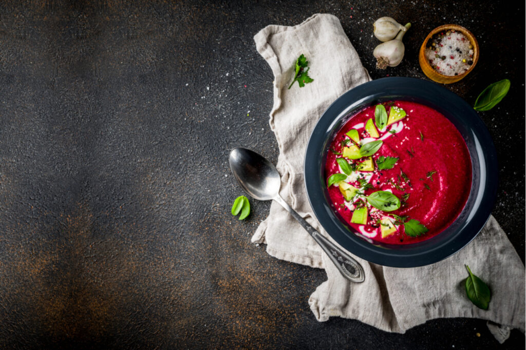 Vegan food, summer cold Beetroot gazpacho soup with lemon, avocado and fresh herbs copy space top view.