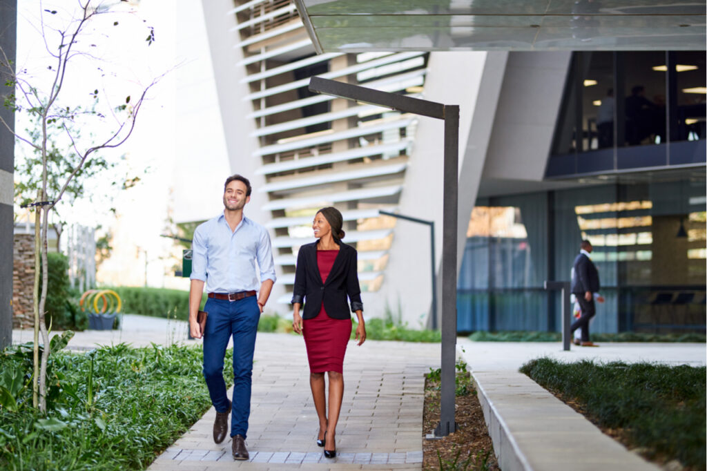 Colleagues smiling and talking while walking together on the grounds of an office complex.