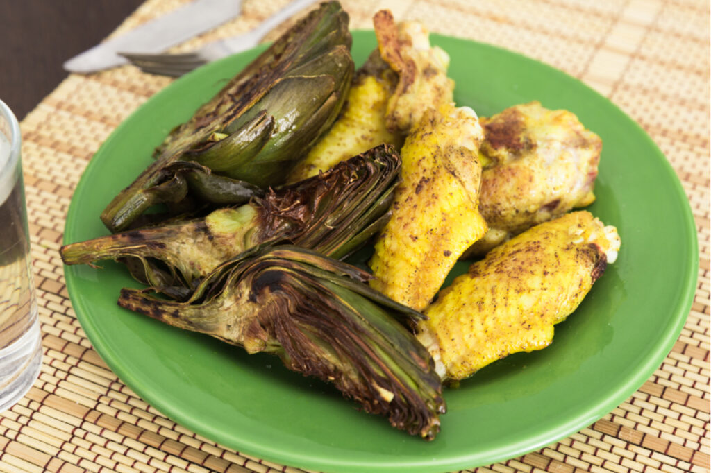 Delicious cooked fried chicken wings and halves artichokes on green plate.