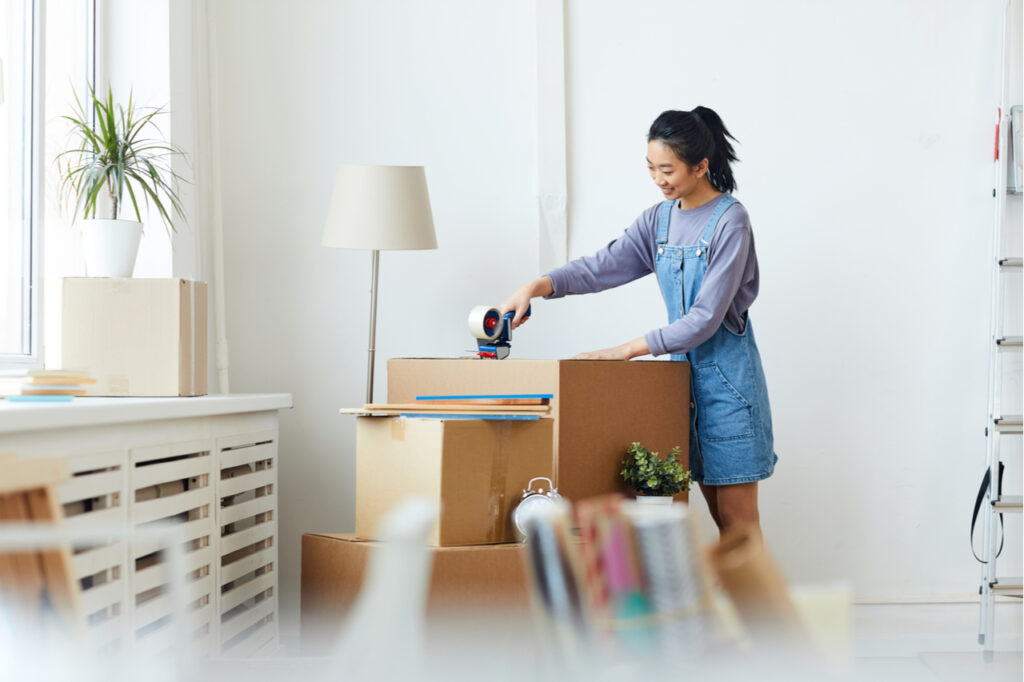 Side view portrait of young woman packing cardboard boxes and smiling happily.