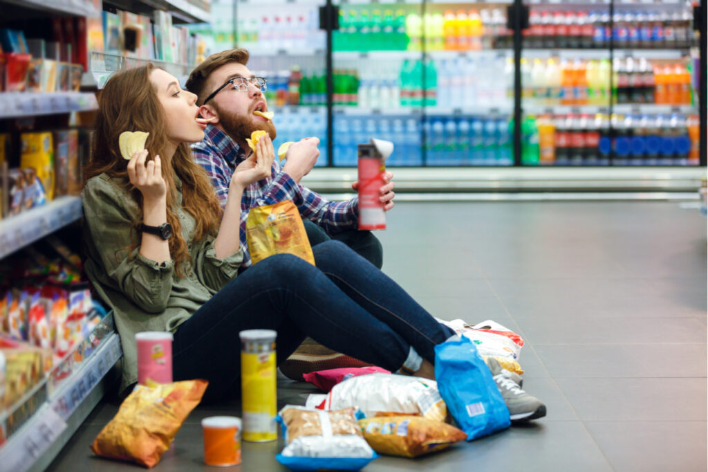 Young couple eating junk foods in a grocery isle. Avoid junk foods for cancer prevention.