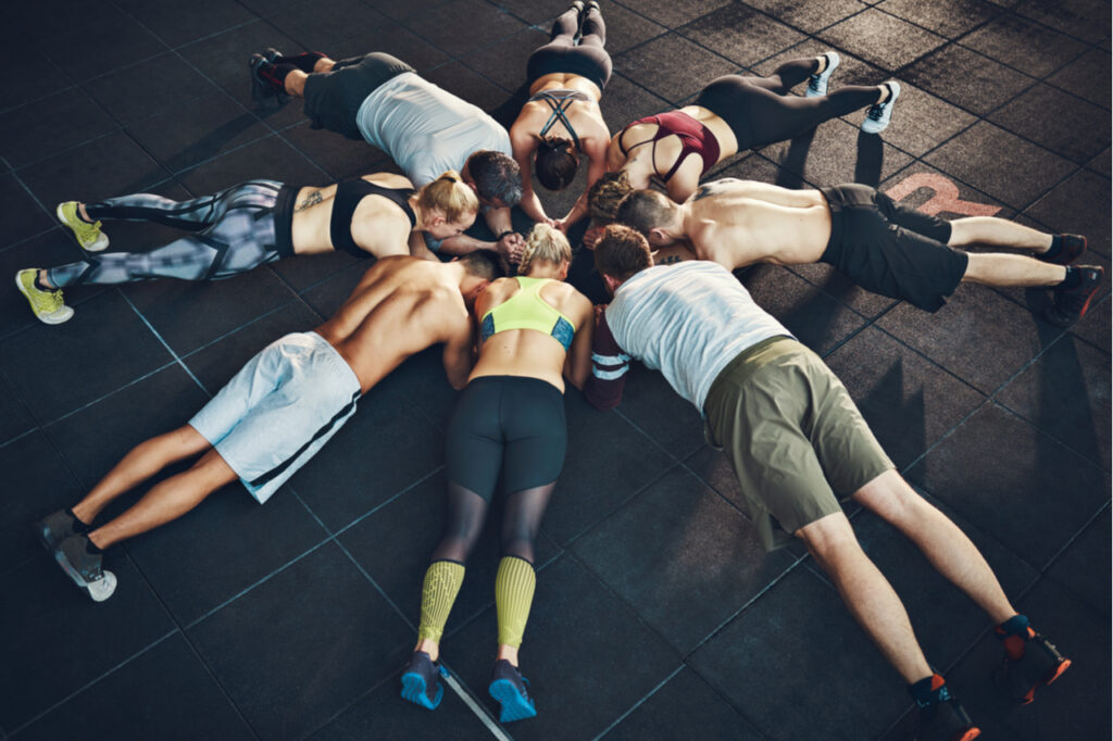 Fit young people focused on planking in a circle in a gym.