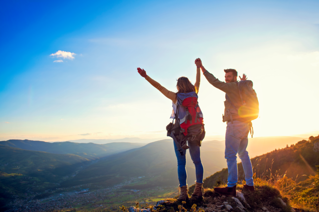 Happy couple man and woman tourist at top of mountain at sunset outdoors.