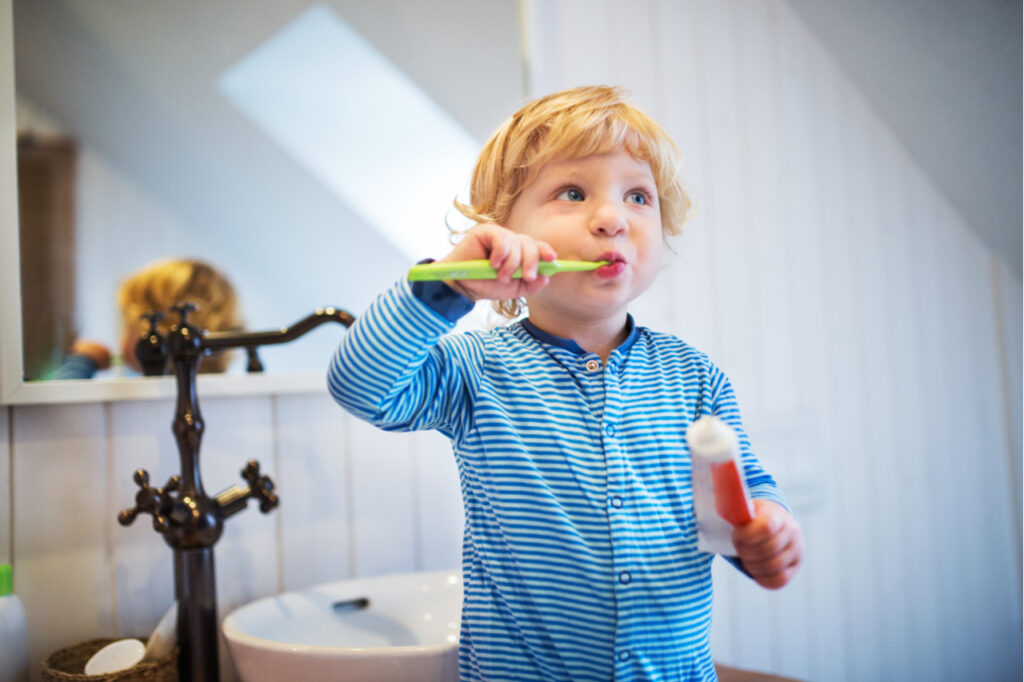 Cute toddler boy brushing his teeth in the bathroom. How to give a kids smile day?