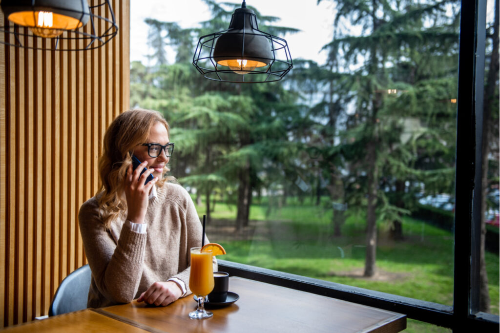 Young charming woman calling with cell telephone while sitting alone in coffee shop during free time.