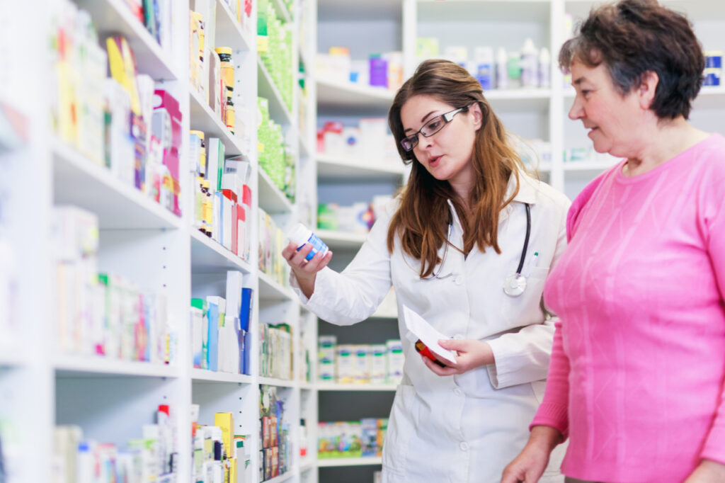 Female pharmacist discusses prescription medication with senior customer at pharmacy for over the counter medicine.