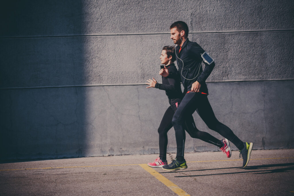 Side view of couple running in an urban environment to prevent cancer.