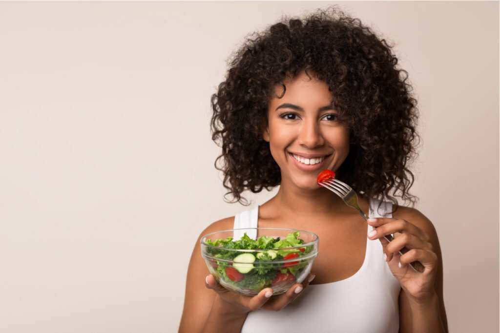 Woman eating vegetable salad over light background.