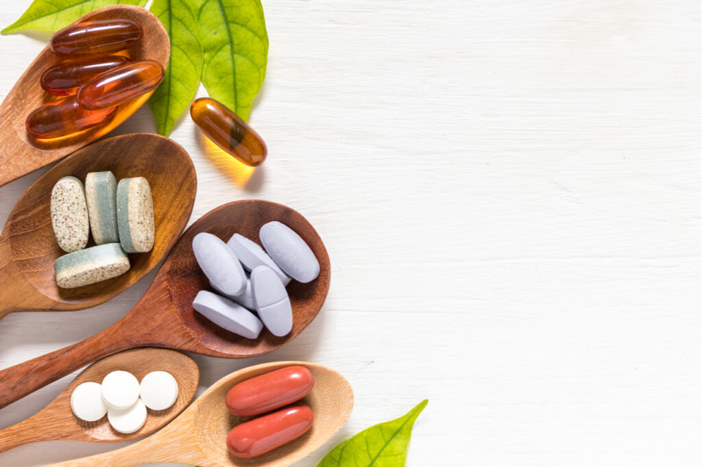 Variety of vitamin pills in wooden spoon.