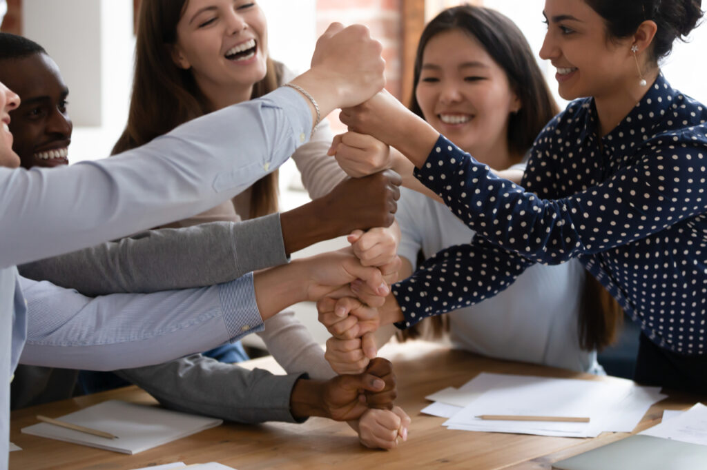 Overjoyed diverse multiracial young people stack fists engaged in funny teambuilding.