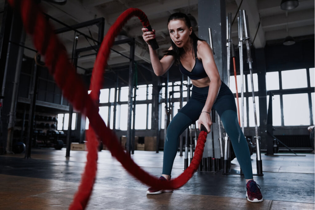 Fit woman using battle ropes during strength training at the gym. Athlete moving the ropes for burning fats at health club.