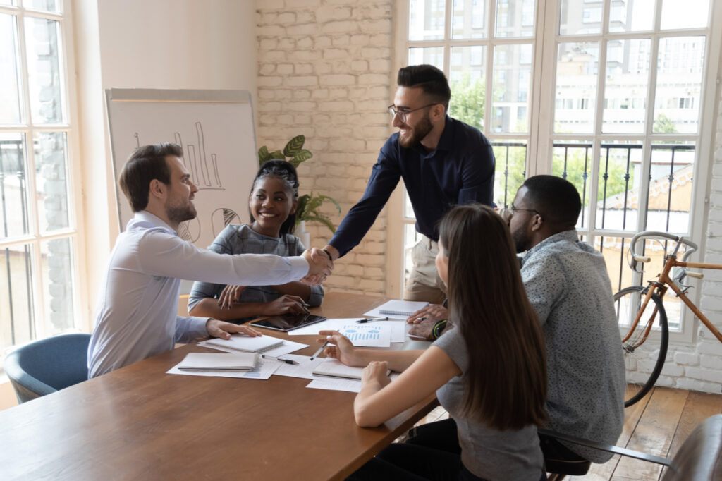 Happy millennial multiethnic male colleagues handshake greeting get acquainted at meeting in office.